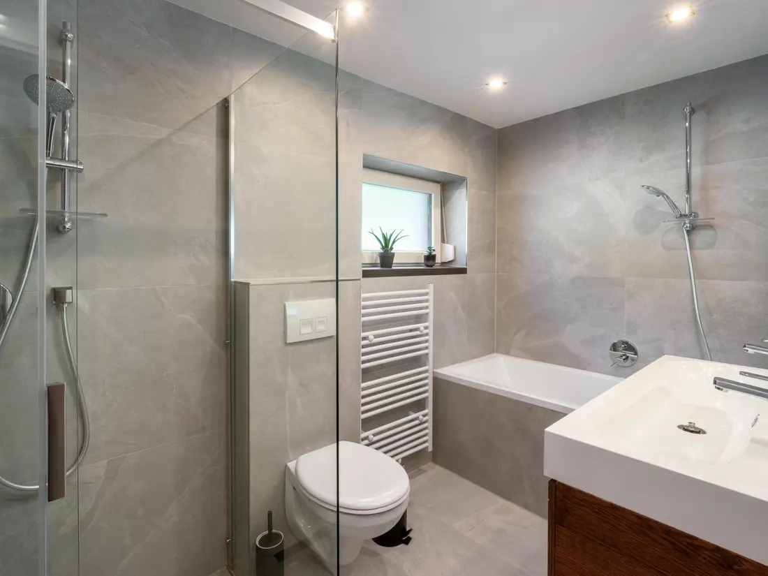 Een badkamer met grijze tegels, een inloopdouche, een ligbad en een wastafel.