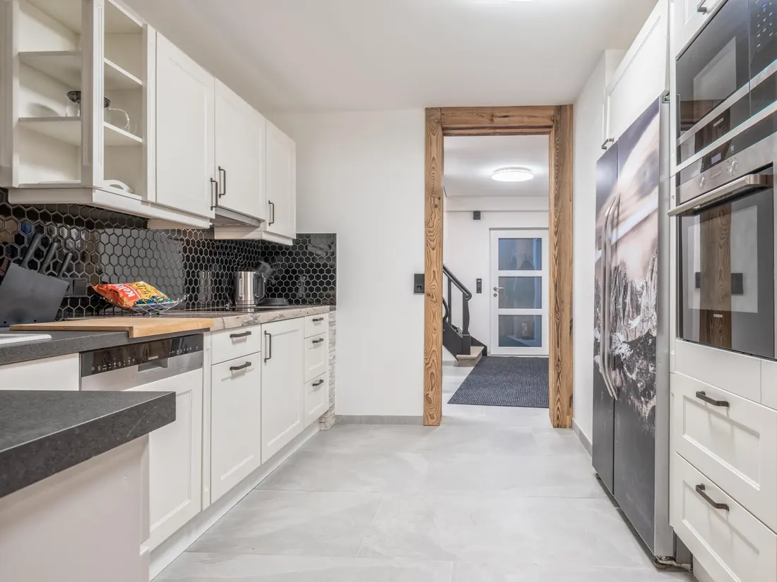 De keuken vanaf de andere kant, met een rij witte kasten, een vaatwasser en een houten balk in de doorgang naar de hal.