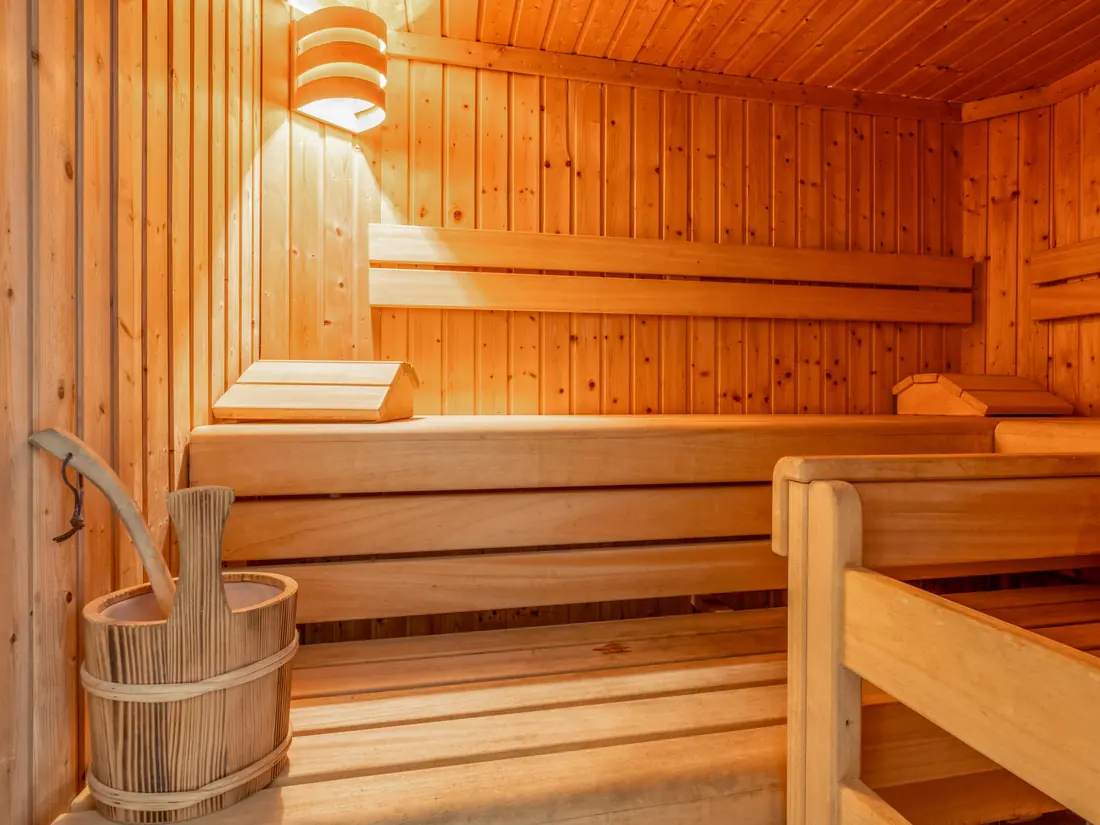 De sauna met houten banken, een emmer en een opgietlepel.